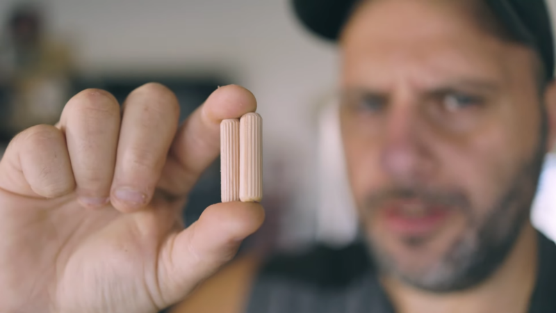 A Man Holds a Wooden Dowel up To the Camera, Illustrating the Selection of The Correct Size for Filling Screw Holes in Woodworking Projects