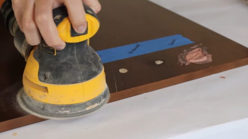 A Person Is Using a Yellow Orbital Sander to Smooth the Surface of A Cabinet Door After Applying Wood Filler to Screw Holes