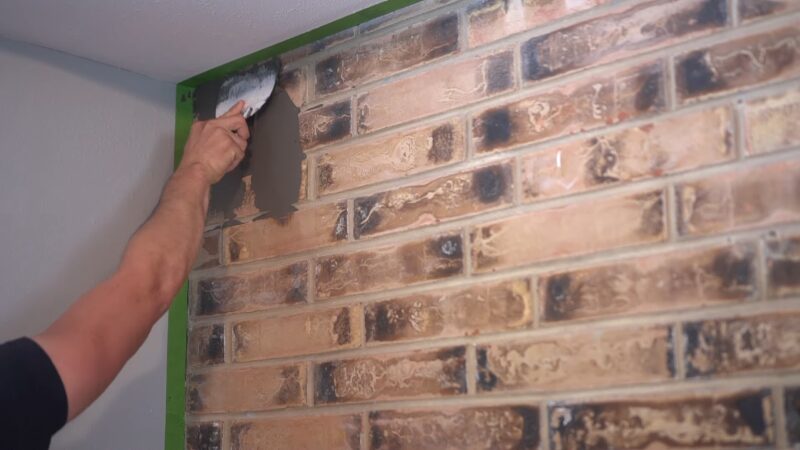 A Person Applying a Thin Layer of Mortar on A Brick Fireplace Wall to Prepare It for Tiling