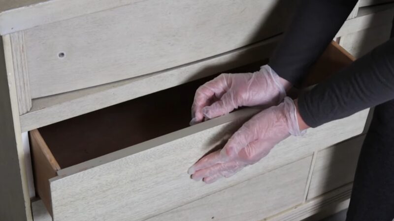 A Person Wearing Gloves Is Opening a Drawer of A Distressed Wood Cabinet, Demonstrating how To Fill Screw Holes with Wood Filler