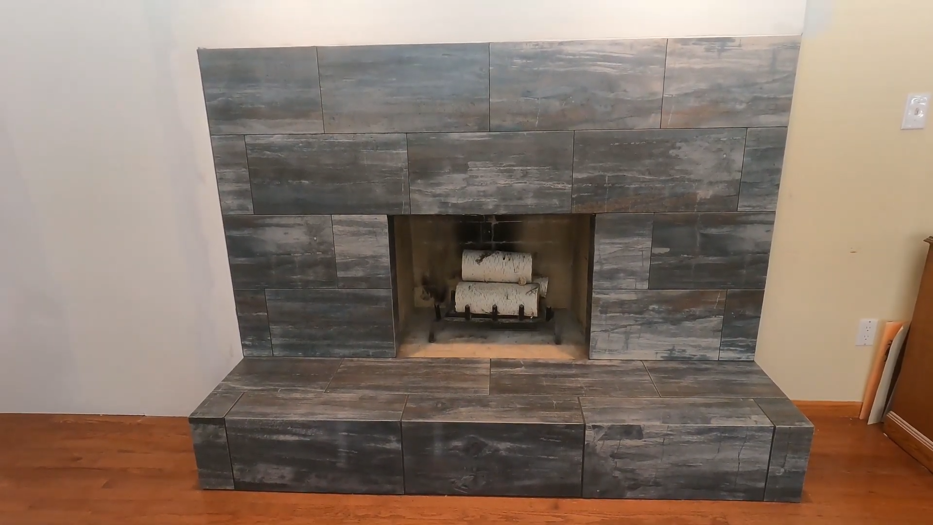 A Fireplace Updated with Dark Gray Wood-Look Tile Over the Original Brick Structure