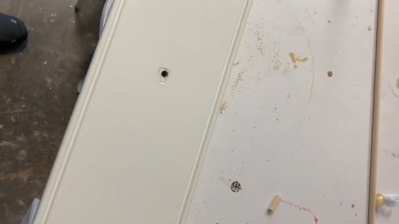 A Close-Up View of A White Cabinet Door with Visible Screw Holes and Dust, Ready for The Application of Wood Filler