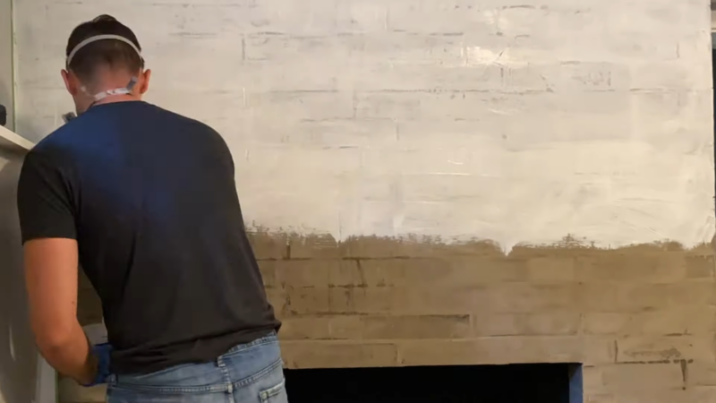 A Man Applying a Thick Coat of White Adhesive on A Brick Fireplace Surface to Prepare for Tile Installation