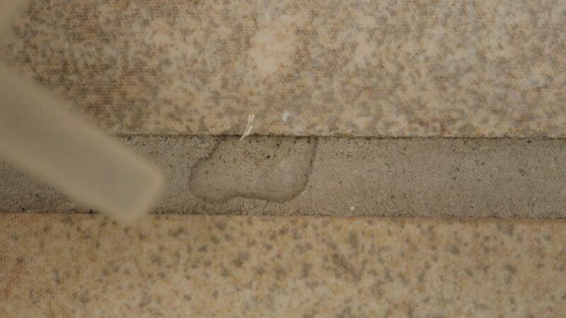 Close-Up of A Caulking Gun Applying Sealant to The Joints Between Beige Tiles