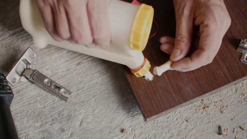 Hands Applying Glue to A Wooden Dowel Before Inserting It Into a Screw Hole in A Cabinet Door to Secure It