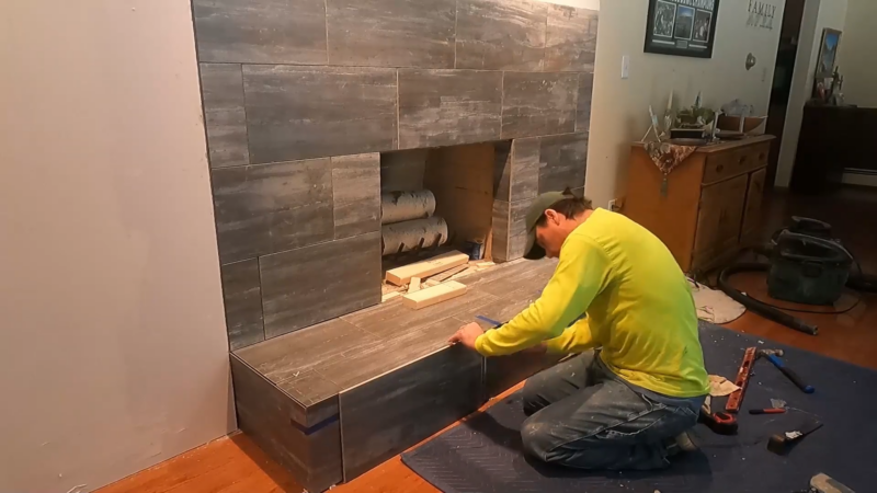 A Man Installing Tile on A Fireplace Surround Using Tools and Materials Laid out On the Floor