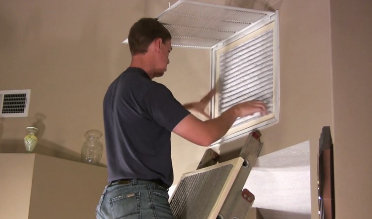 A man installs a window air conditioner, carefully positioning it in the window frame for proper fit and support