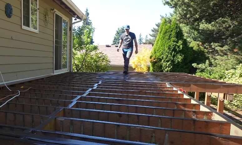 A man walks on a wooden deck beside a ladder, suggesting a construction activity